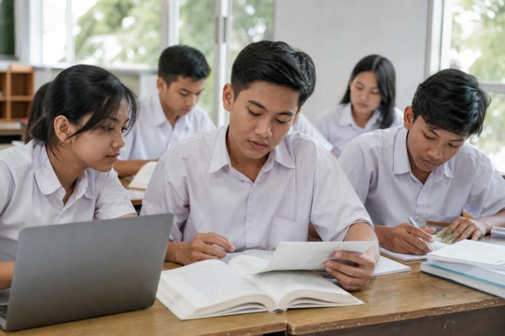 Pelajar membandingkan informasi dari buku dan laptop di ruang kelas